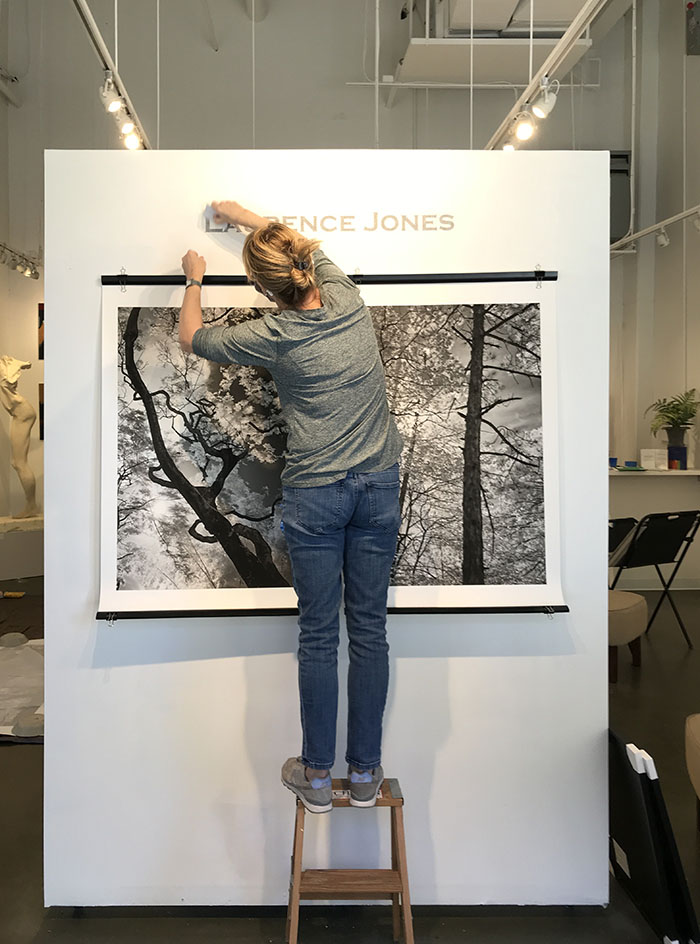 Martha Spak on Short Step Ladder Lettering over Two Large Photos in the Entrance to Her Gallery.